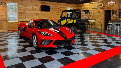 Corvette and ATV in a garage with RaceDeck Diamond. The floor has a checkerboard pattern with a red border. There's wood paneling on the wall.